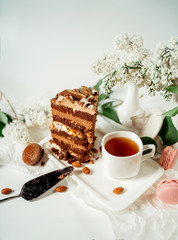 Chocolate cake decorated with various cookies and nuts on a glass plate and macaroons among white flowers of lilac and green leaves. Food photography. Advertising and commercial close up design.