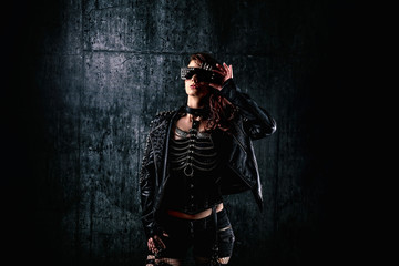 Young woman with scarified face, wearing a studded leather jacket, holding her glasses.