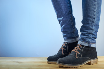Female legs in demi-season boots and blue jeans on wooden floor on a blue background. Fashion background. Photo with copy space.