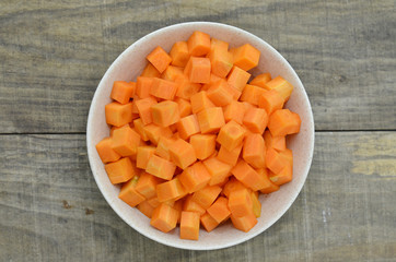 cuts cubes of carrot in bowl on wooden background