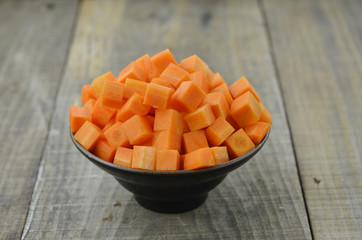 cuts cubes of carrot in black bowl on wooden background