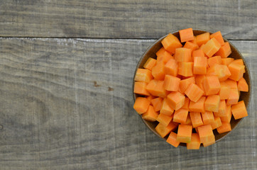 cuts cubes of carrot in black bowl on wooden background