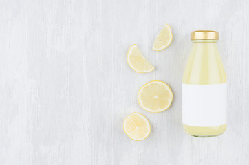 Organic lemon yellow juice in glass bottle with blank label, sliced citrus on white wood...
