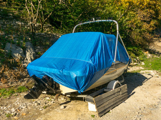 A small boat, sheltered by an awning is prepared for transportation on the background of fruit trees