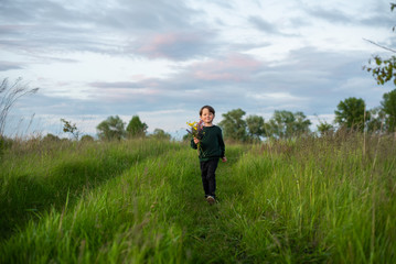 Naklejka na ściany i meble Little smiling boy carries a bouquet of wildflowers in the field