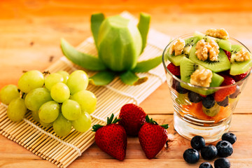 Close-up view of a mixed and fresh colorful fruit salad in a glass cup. Fresh fruit on the background on a wooden table