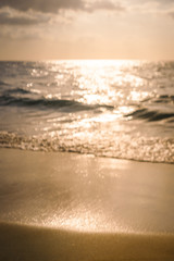 Blur background of sea waves hit the coast causing white bubbles and splashes of water. The orange color glow of the sunset creates warm tones. Sandy beaches with glistening. There is copy space.