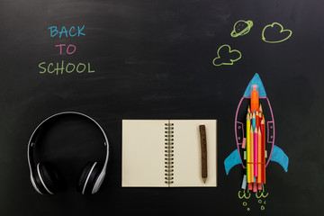 Education or back to school Concept.Top view of headphone, notebook and painted rocket with colorful of color pencil and chalk on chalkboard background,Copy space for text.Flat lay