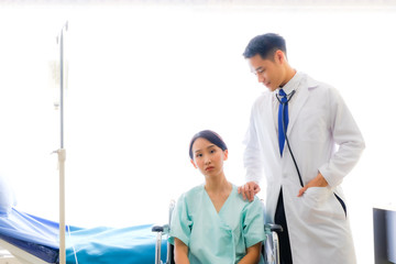 Close up Asian male Doctor explaining diagnosis to his female patient is sitting a wheelchair with anxiety. Doctor discussing test results with the patient, in the hospital/ coronavirus, Covid-19.