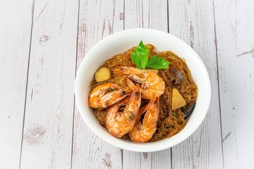 Casseroled shrimps roasted with glass noodles or prawns with Vermicelli Noodles in white blow with chinese celary on the top view. Asian Food Thai fusion style. famous food in Thailand national dish.