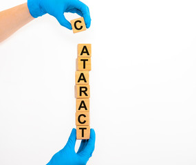 Text word inscription CATARACT on wooden cube blocks in hands in protective medical gloves on white...