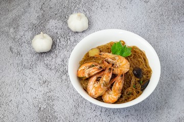 Casseroled shrimps roasted with glass noodles or prawns with Vermicelli Noodles in white blow with chinese celary on the top view. Asian Food Thai fusion style. famous food in Thailand national dish.