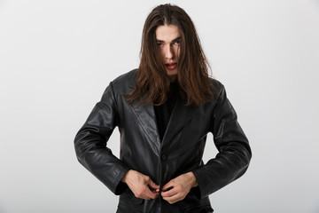 Portrait of brunette young man with long hair wearing black lather jacket posing and looking at...