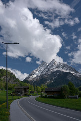 Peak of the mountains in the clouds on a background of blue sky. and the road in the village.