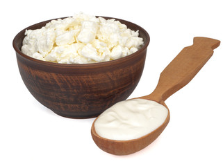 Fresh homemade cottage cheese in a bowl and a spoon with sour cream on white background