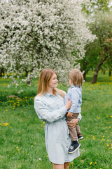 Fototapeta premium Mom with a child plays in the garden. Mom and son walk in the park. Relations between mom and son.