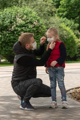 Little blonde girl with her father in medical masks in the park