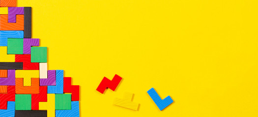 Different colorful shapes wooden puzzle blocks on yellow background. Top view