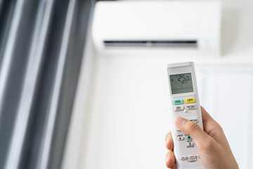 Human hand is using white remote of air conditioner for turn on or adjust temperature of air conditioner inside the room.