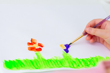 Child is drawing flowers by watercolors on white paper. Children's and Earth day concept.