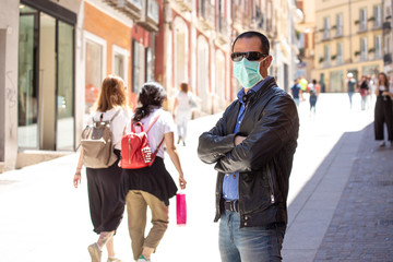 Obraz premium Uomo vestito casual e con mascherina fermo nel marciapiede di una città con paesaggio persone sullo sfondo