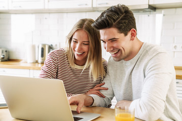 Portrait of couple using laptop and smiling while having breakfast