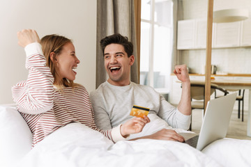 Portrait of excited couple holding credit card while using laptop