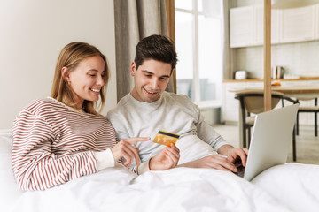 Fototapeta premium Portrait of couple holding credit card and using laptop while lying