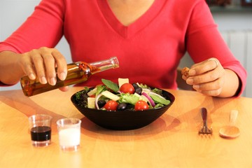 Woman hands holding olive oil bottle and the cork preparing her diet  Mediterranean salad bowl on wood table. photo front view 