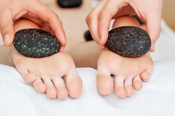 Close up of hands of masseur making foot massage with hot stones.