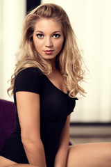 Fototapeta premium Blonde junge Frau mit Locken in Body Dessous sitzend im Sessel