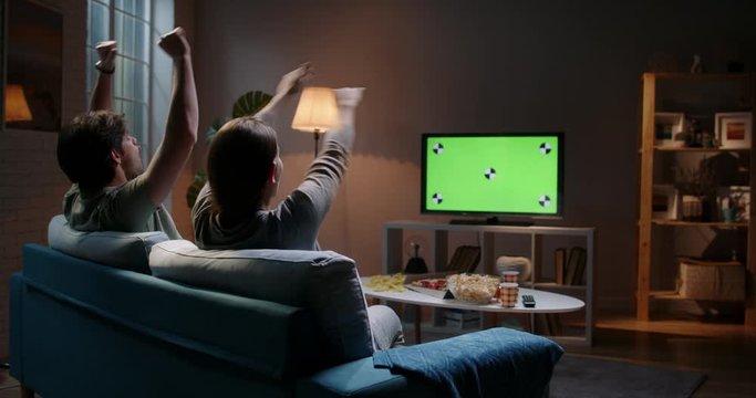 Emotional sports fan couple spending time together watching chroma-key green screen tv and reacting to their team play. 4k footage template