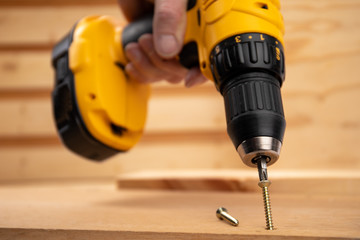 a male hand holding a  yellow battery operated drill with a screwdriver bit in a construction...