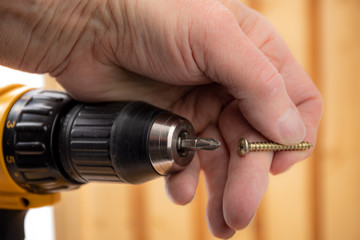 closeup of a male hand placing a screw on a screwdriver bit in an electric drill