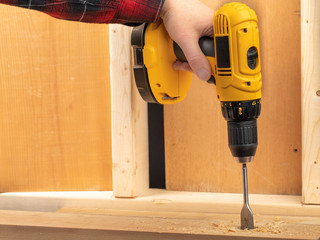a male hand holding a  yellow battery operated drill with a screwdriver bit in a construction...