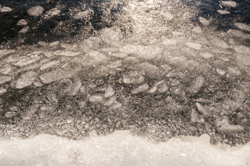 Splashing waves and pieces of ice in lake water, sunny winter day