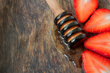 
strawberries on a wooden plate with honey dipper and transparent linden honey.