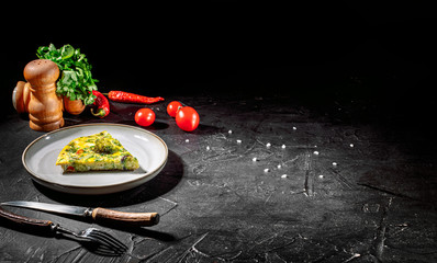 Tasty frittata with spinach and herbs in an iron frying pan on an dark background. Fritatta with broccoli