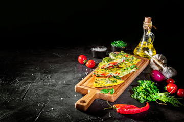 Pieces of tasty frittata with spinach on table on a dark background. Delicious frittata with spinach and herbs