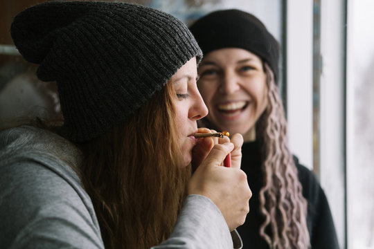 Female friends wearing hats and rasta dreadlocks hair style smoking self-roll weed cigarette