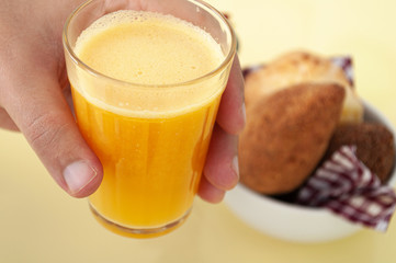 holding a glass of orange juice and brazilian snacks on a yellow background