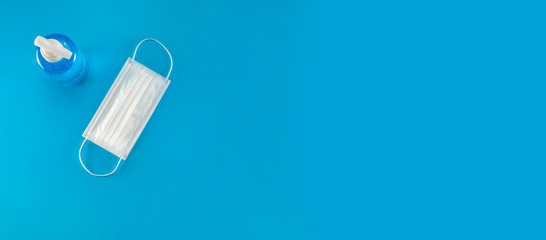 Top view medical face mask and alcohol gel on light blue background with copy space. Face mask and hand sanitizer gel in pump head bottle.
