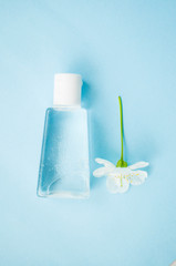 Hand antiseptic bottle and beatiful blooming cherry tree flower on blue background. Stop coronavirus concept.