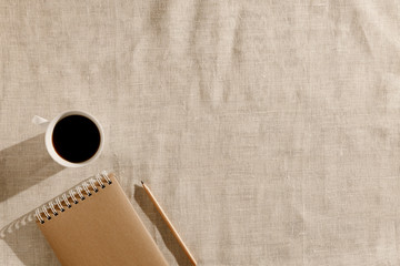Blank brown vintage sketchbook, pencil, cup of coffee on beige linen fabric in the morning....