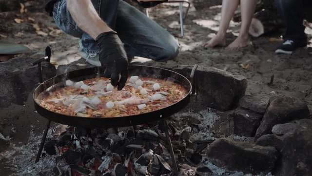 Closeup mans cook paella in a large frying pan outside, field kitchen, catering