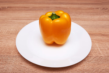 Colorful yellow bell peppers in a white plate on wooden table. Top view with copy space. flat lay