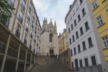 Old church in the middle of urban city and people are staying in front of tower with touristic guide. Cityscape of houses urban architecture with history concept in Vienna, Austria.