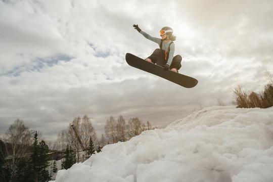 Snowboarder woman jumping from kicker in winter cloudy day