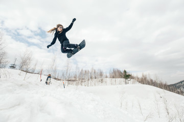 Snowboarder woman jumping from kicker in winter cloudy day