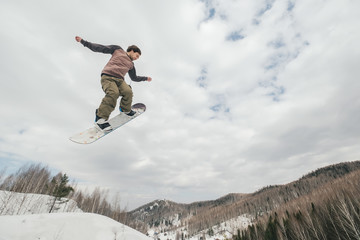 Fototapeta na wymiar Snowboarder jumping from kicker in winter cloudy day